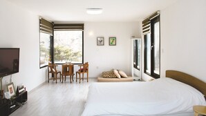 A bedroom with a bed, a desk with chairs, a TV, and a window with blinds.