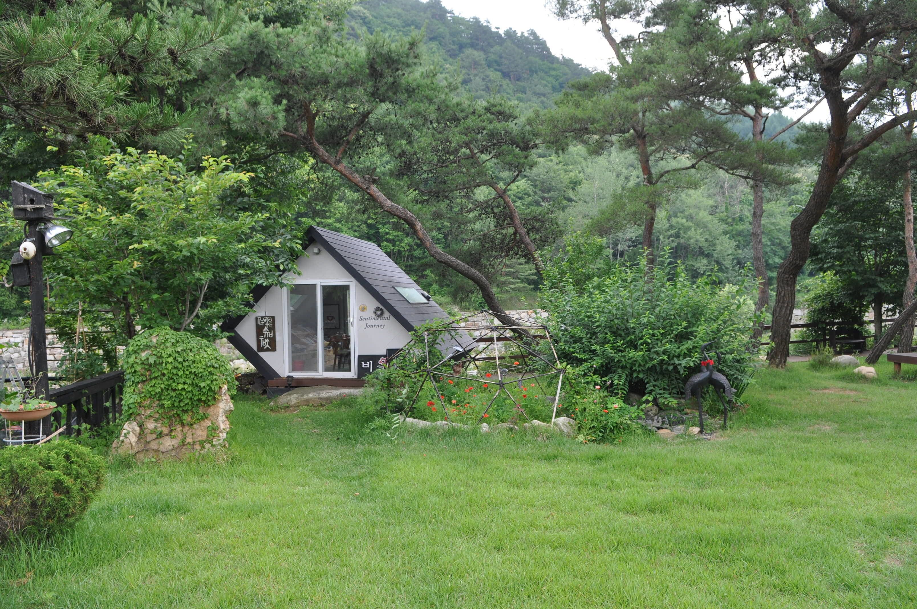 A small house with a sloped roof, surrounded by lush greenery and trees.