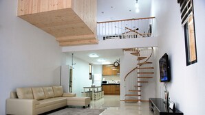 A spacious living area with a beige sofa, a small coffee table, a staircase leading to an upper level, and a kitchen in the background.