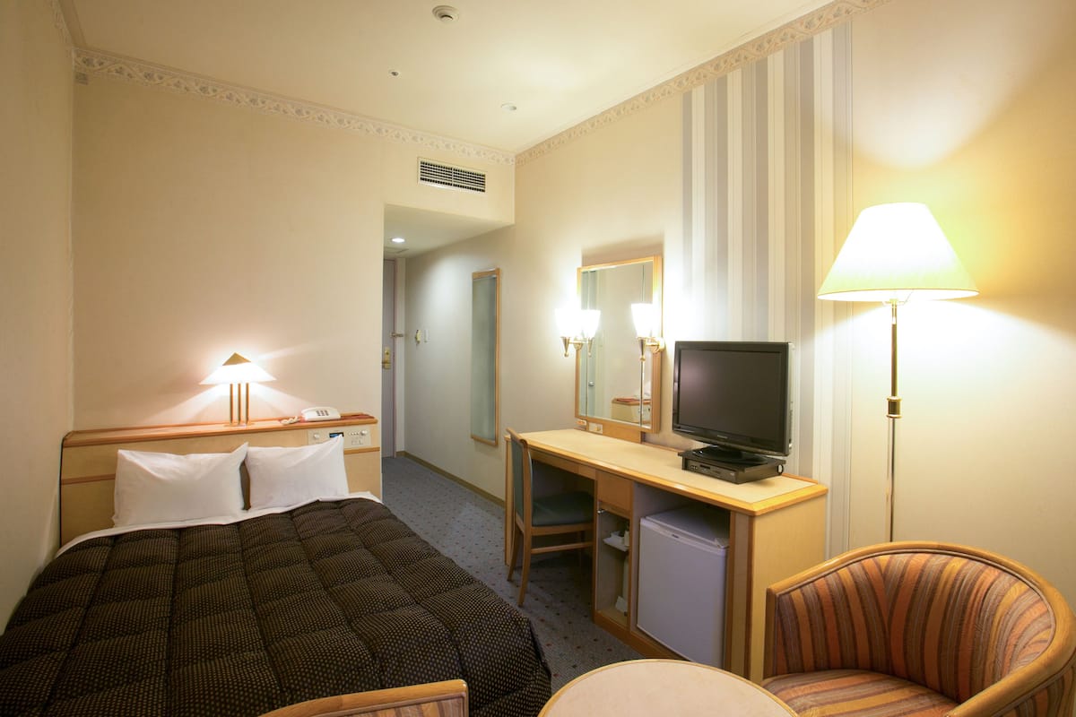 Une chambre d’hôtel comprenant un lit, un bureau avec une télévision, une chaise et une lampe.
