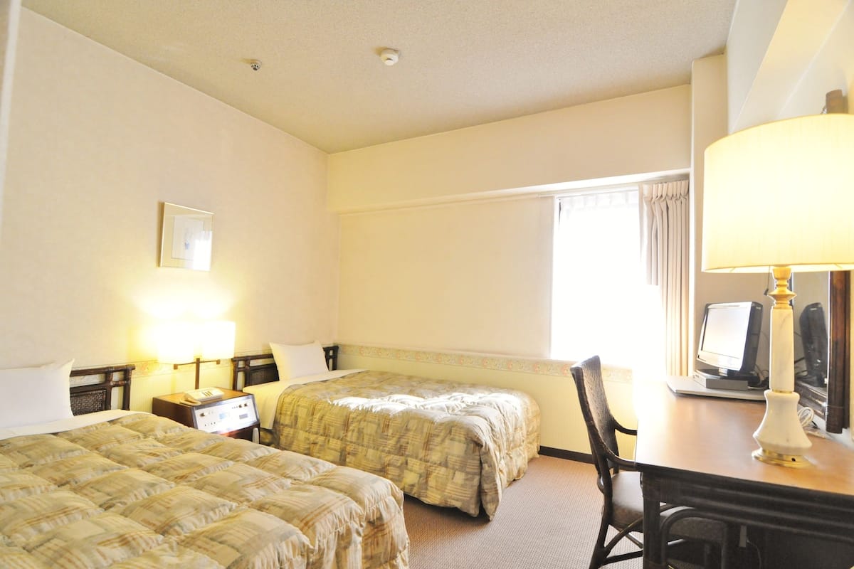 Une chambre d’hôtel avec deux lits, un bureau avec un ordinateur et une lampe.