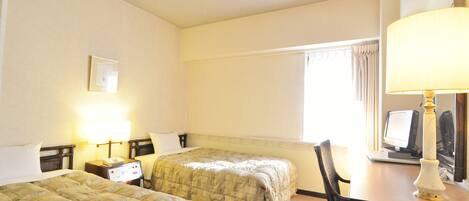 A hotel room with two beds, a desk with a computer, and a lamp.