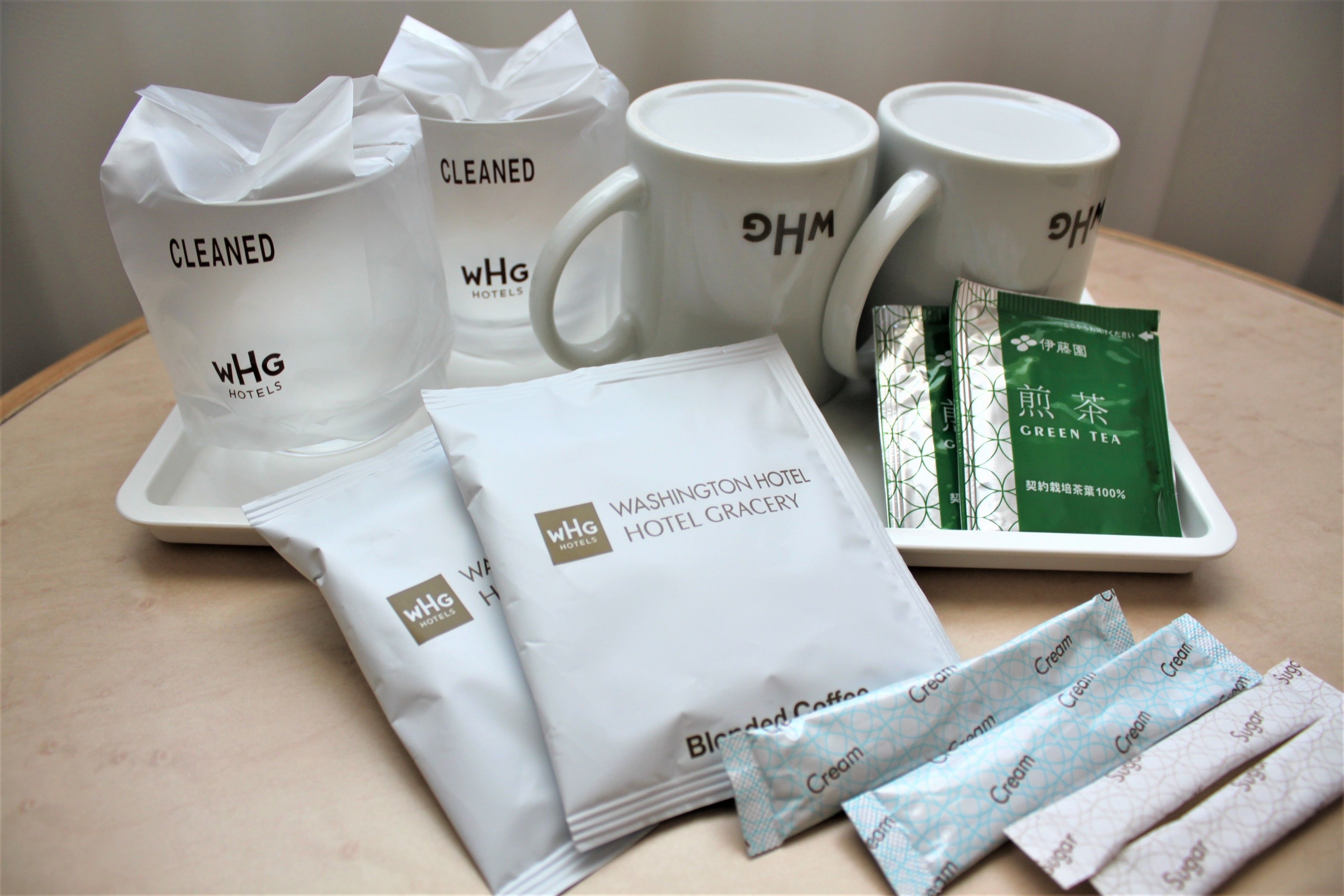 A tray with hotel amenities including bags labeled "WHG Hotels," a tray of green tea, and white mugs with "WHG" logos.
