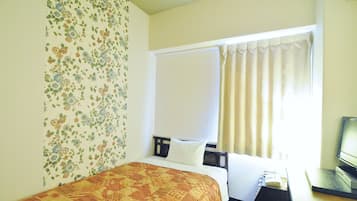 Habitació d'hotel amb un llit, una taula de treball amb un ordinador, una finestra amb cortines i paper pintat floral.