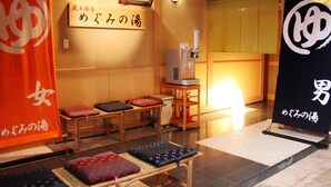 Une pièce de style japonais traditionnel, avec des tatamis, une table en bois et des coussins. On y trouve un panneau avec des caractères japonais et un distributeur d’eau.