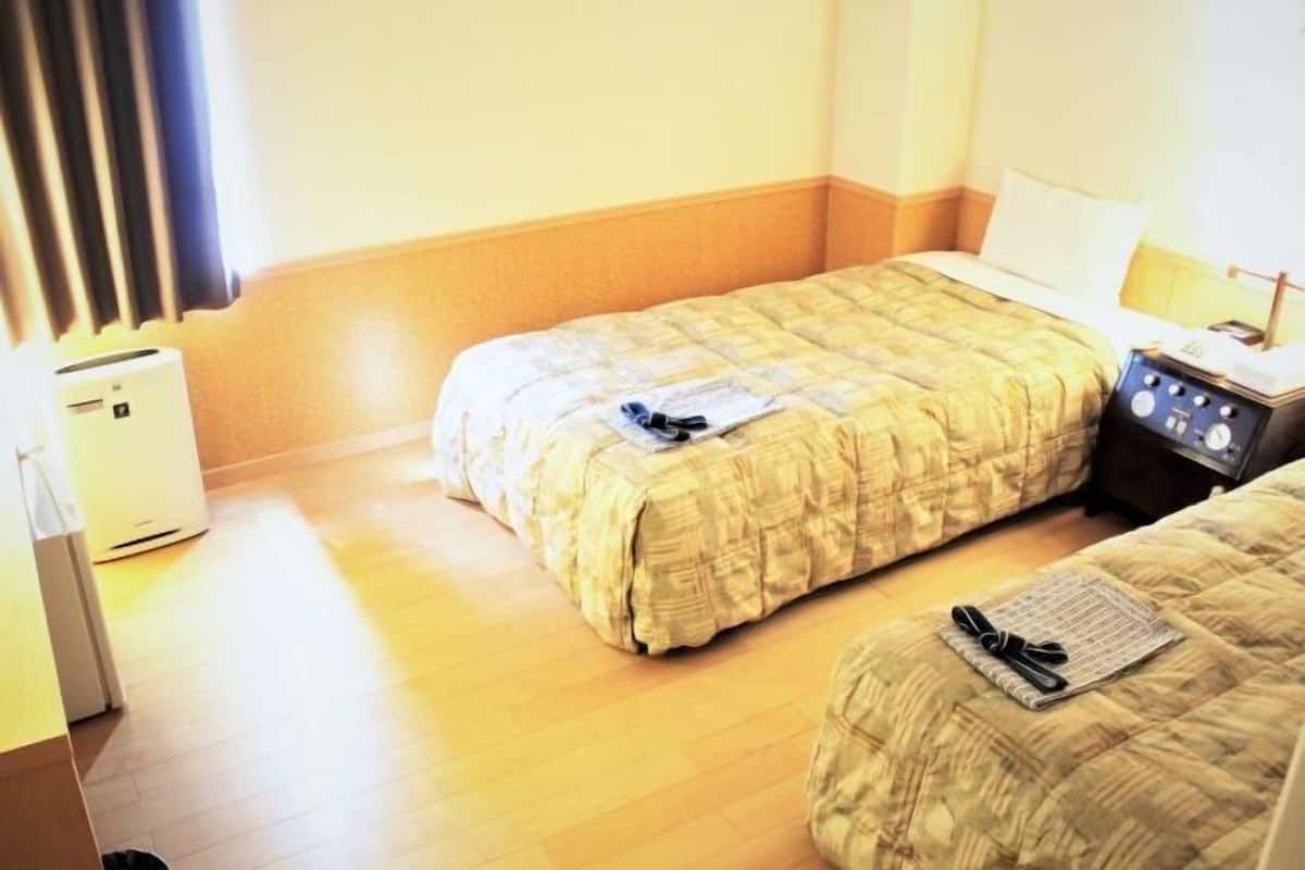 Une chambre d’hôtel avec deux lits, une table de chevet avec une lampe, un radiateur et une petite table avec un carnet et un stylo.