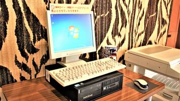 A desktop computer with a keyboard and mouse on a wooden desk, a printer, and a patterned wall in the background.