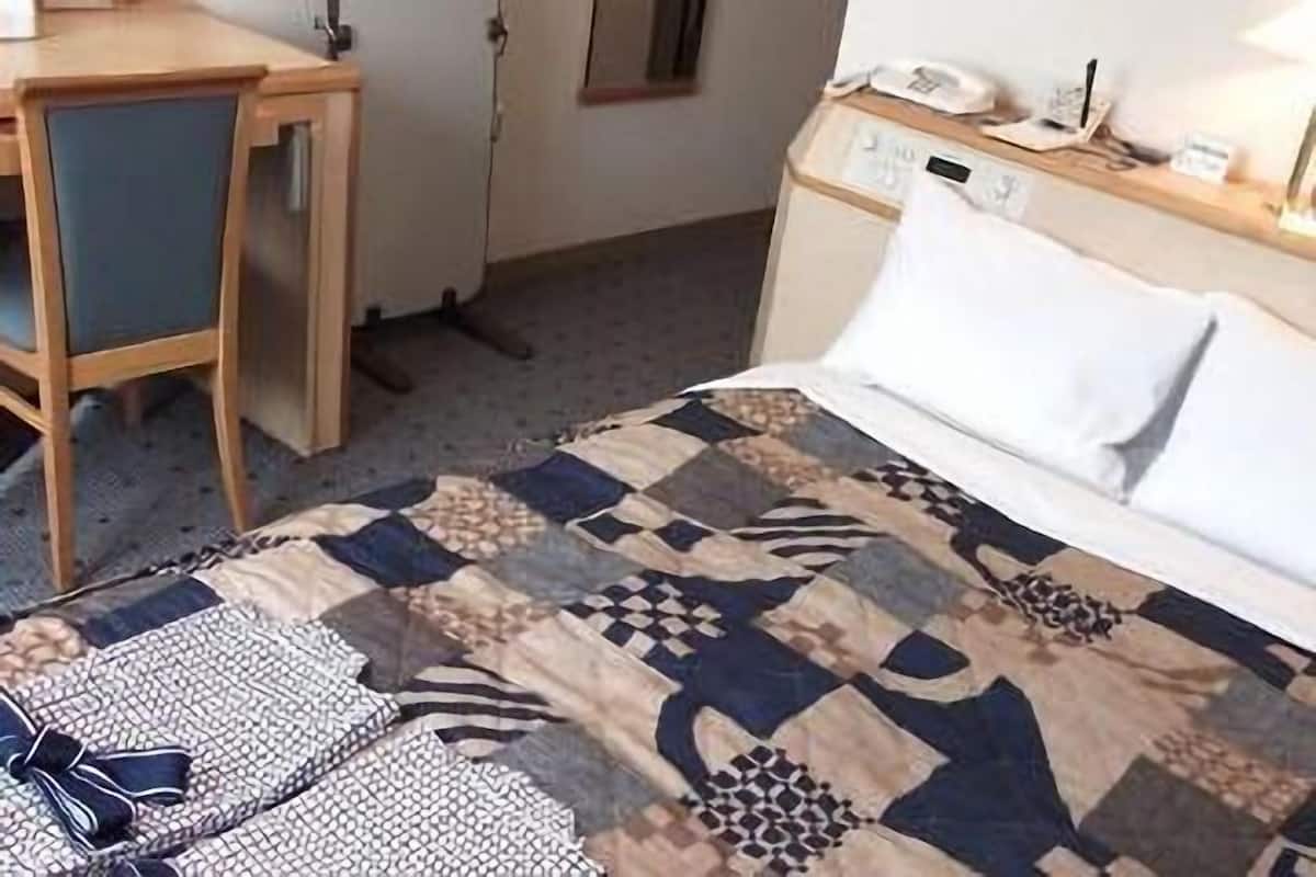 Une chambre d’hôtel comprenant un lit, un bureau, une chaise et une table de chevet avec une lampe.