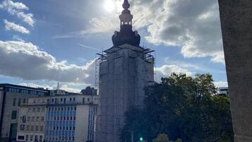 A building with a prominent tower under construction, surrounded by urban buildings and trees.