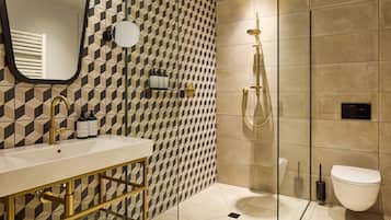 Een moderne badkamer met een geometrisch patroon op de muur, een gouden kraan, een douche met glazen wanden en een wit toilet.