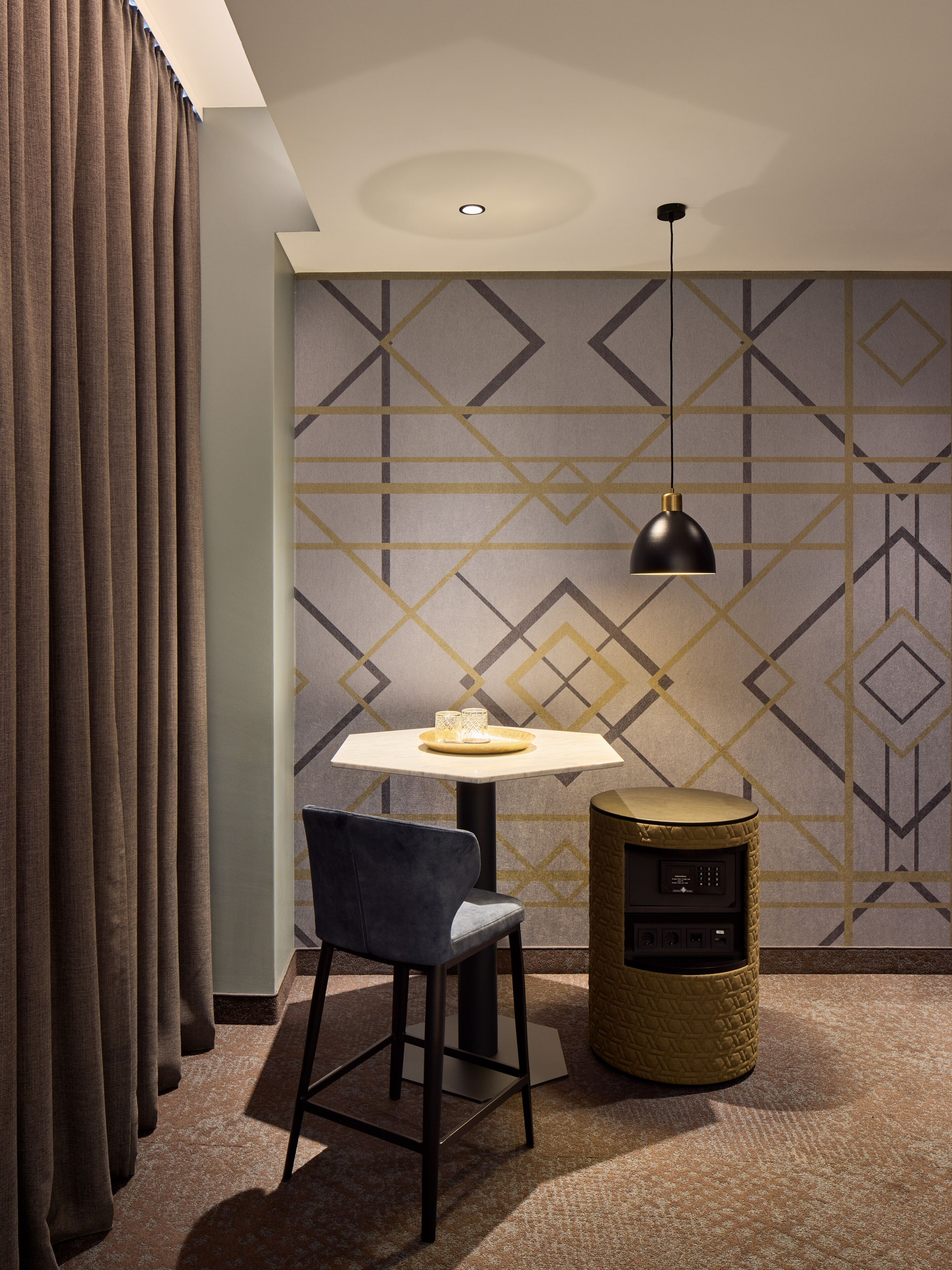 A modern room with a geometric patterned wall, a round table with a chair, a lamp, and a small speaker.