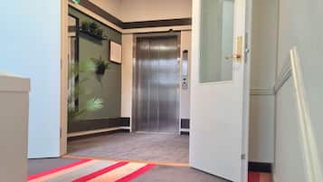 Un ascenseur aux finitions métalliques, une porte dotée d’une poignée et un sol recouvert de moquette à rayures rouges et grises.