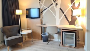 A compact hotel room with a sofa, a desk with a computer, a television, and a small refrigerator. - City Living Sentrum Hotell (Trondheim)
