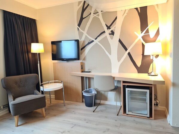 A compact hotel room with a sofa, a desk with a computer, a television, and a small refrigerator. - City Living Sentrum Hotell (Trondheim)