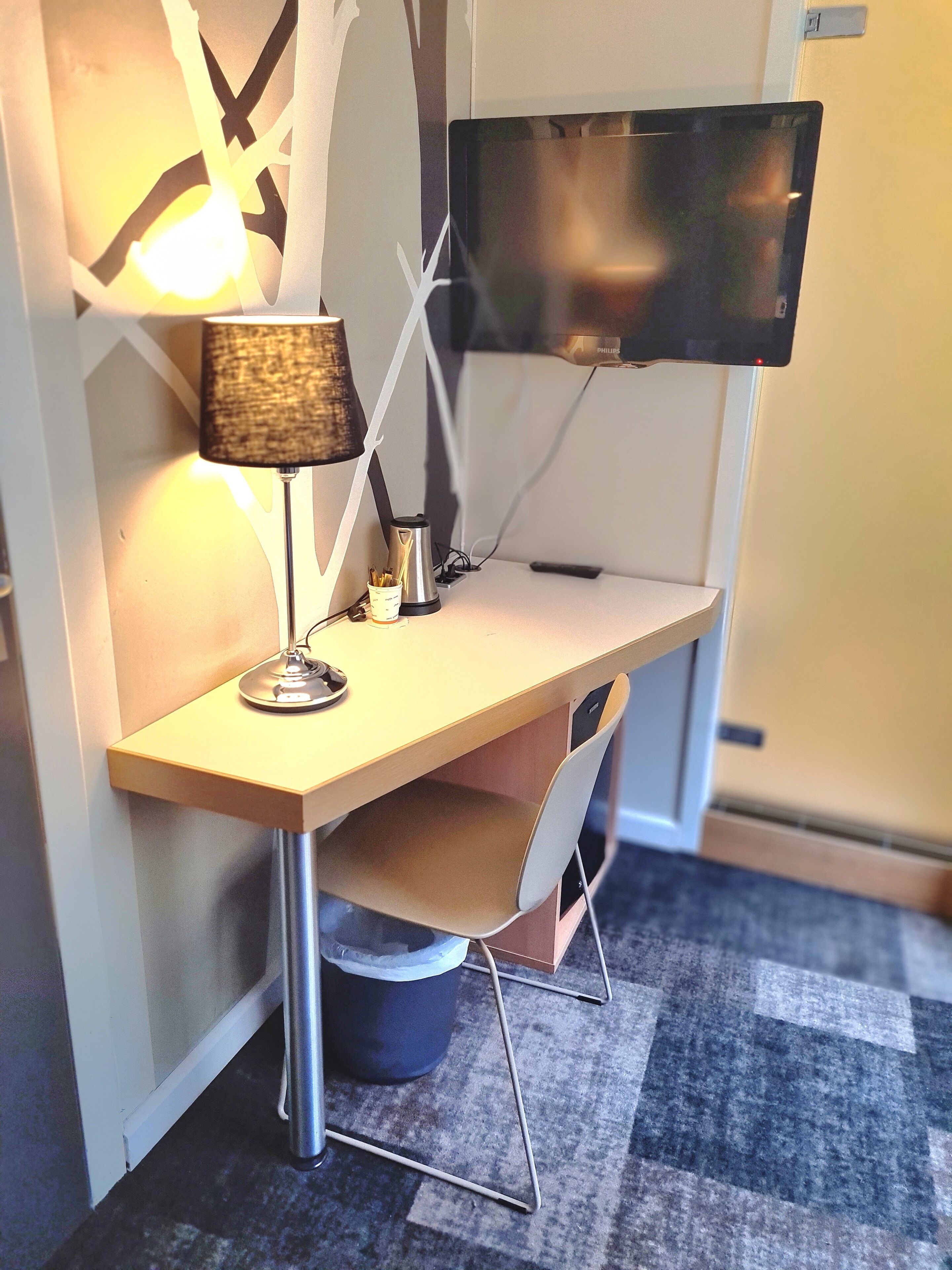 Un petit espace de travail moderne comprenant un bureau, une chaise, une lampe et un téléviseur à écran plat fixé au mur.