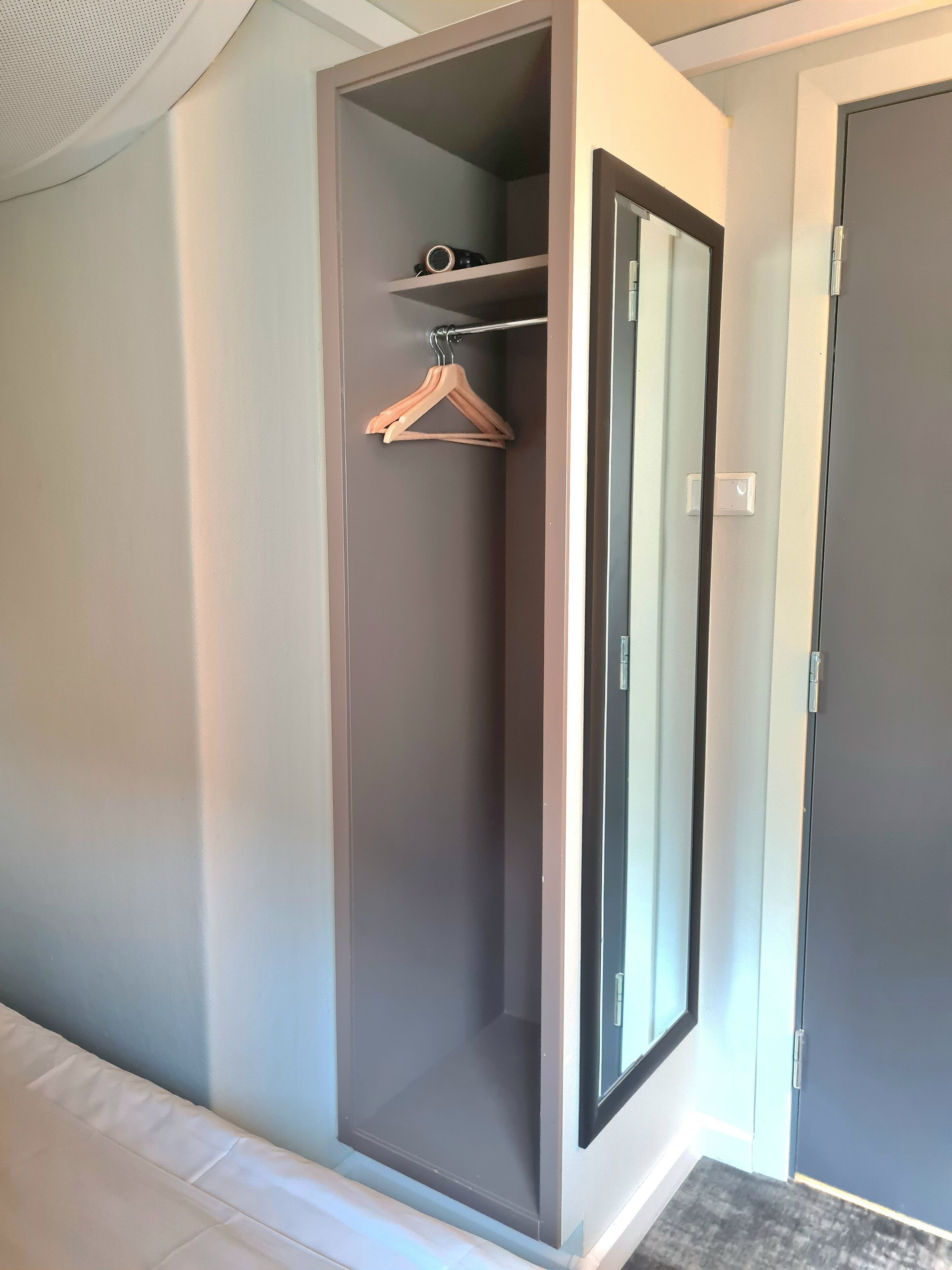 Un vestidor con espejo, perchero y puerta.