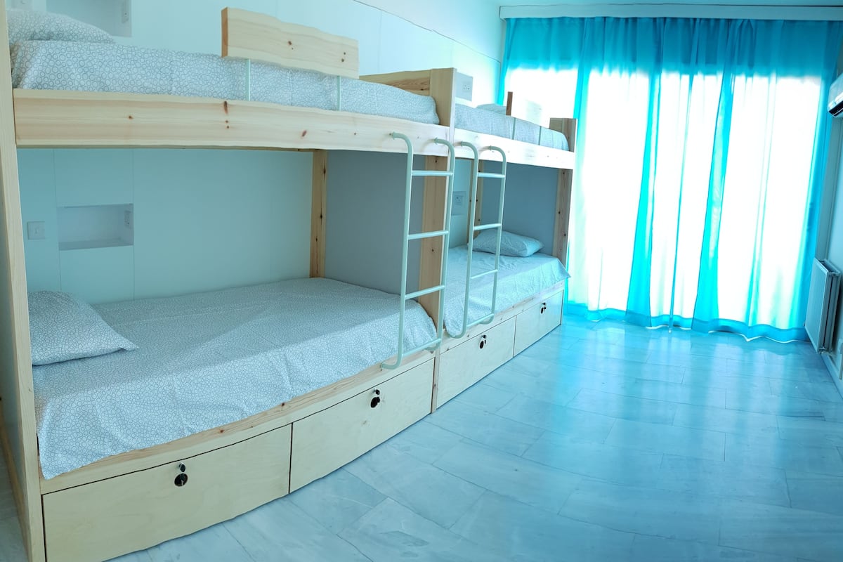 A bunk bed room with a ladder, built-in drawers, and a window with curtains.