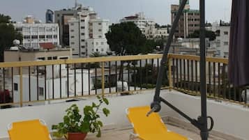 Una terraza en la azotea con sillones amarillos, una planta en maceta y una barandilla metálica.