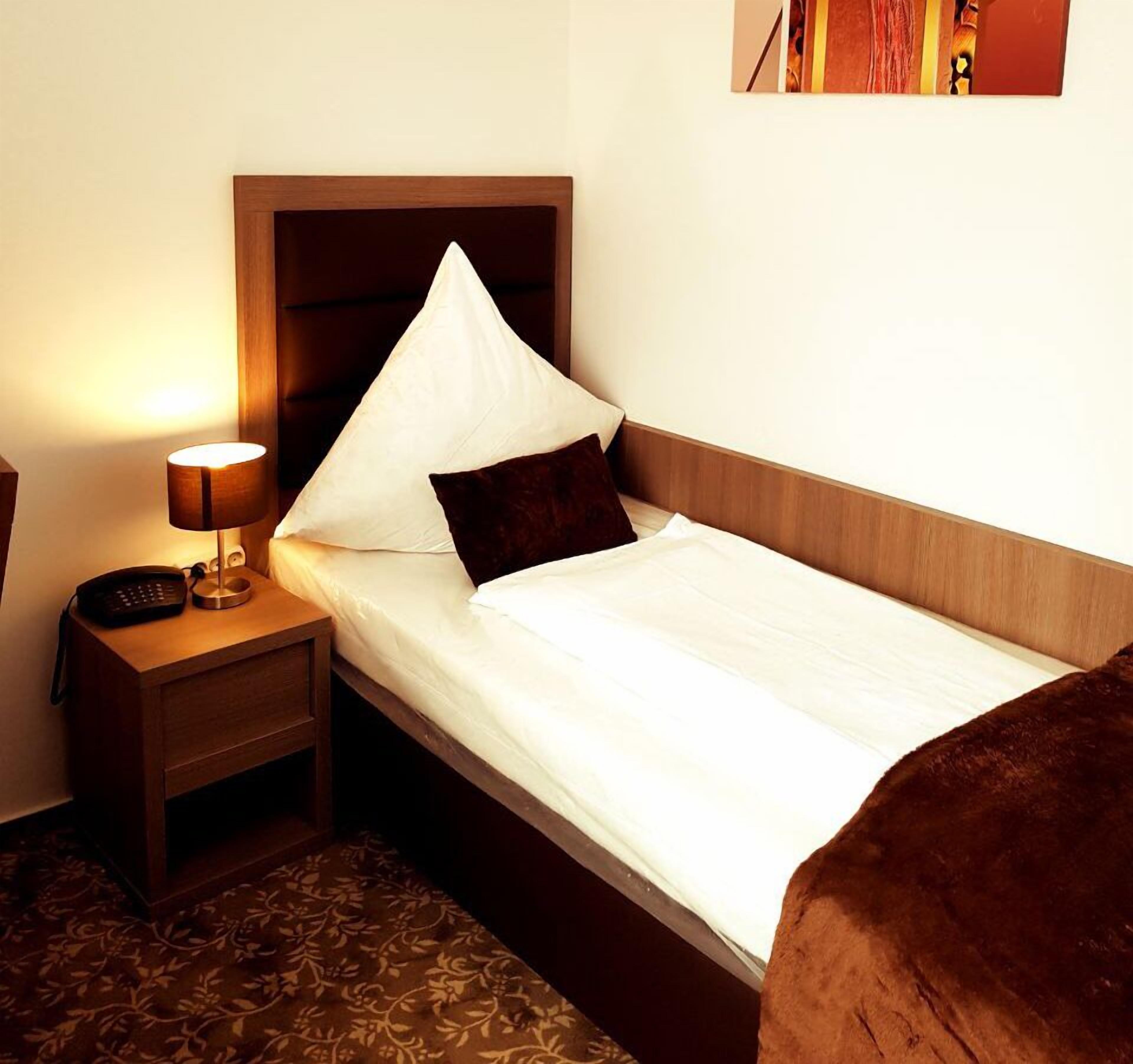 A hotel room with a single bed, a nightstand with a lamp, and a telephone.