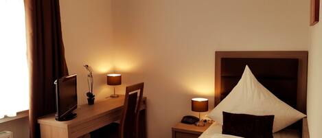 A hotel room with a bed, desk, chair, lamps, and a television.