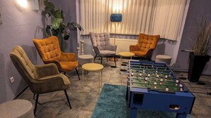 A room with a foosball table, two armchairs, a small round table, and a potted plant. - easy&cosy Hotel Moers (Moers)