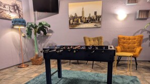 A room with a foosball table, a TV, a plant, and two chairs. - easy&cosy Hotel Moers (Moers)