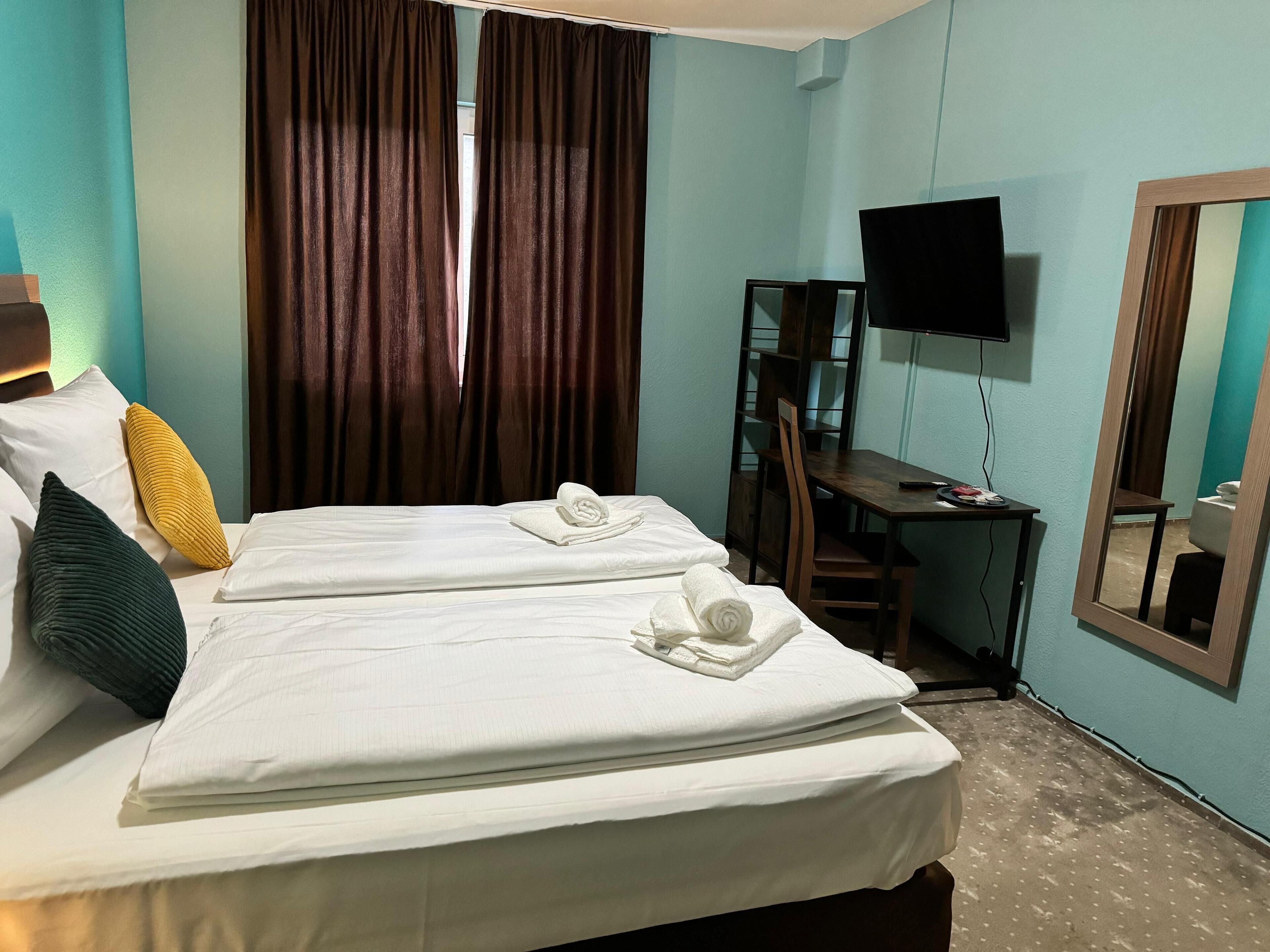 Habitación de hotel con dos camas, un escritorio, una silla, un televisor y un espejo.