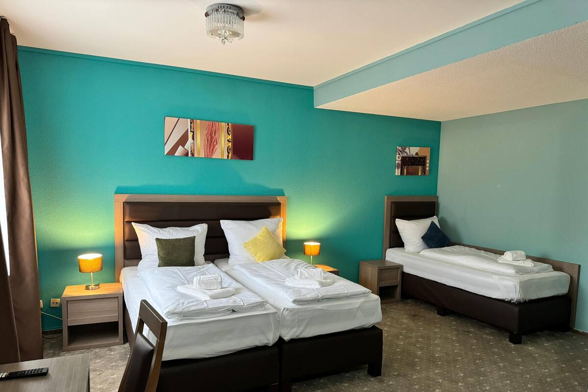 Une chambre d’hôtel avec deux lits, des murs de couleur turquoise, un lustre et des œuvres d’art.