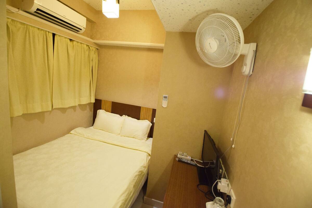 Una habitación de hotel con cama, aire acondicionado, ventilador, televisor y teléfono.
