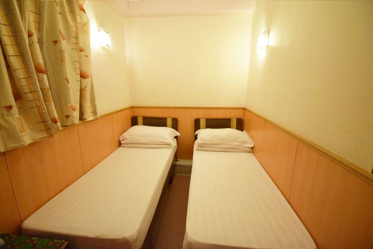 Un alojamiento pequeño y de una sola habitación con dos camas individuales, cabecero de madera y cortina con estampado de hojas.