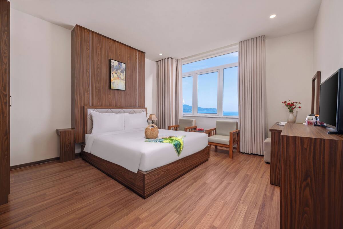 Una habitación de hotel moderna con una cama grande, paneles de madera, un escritorio, una silla y un televisor.