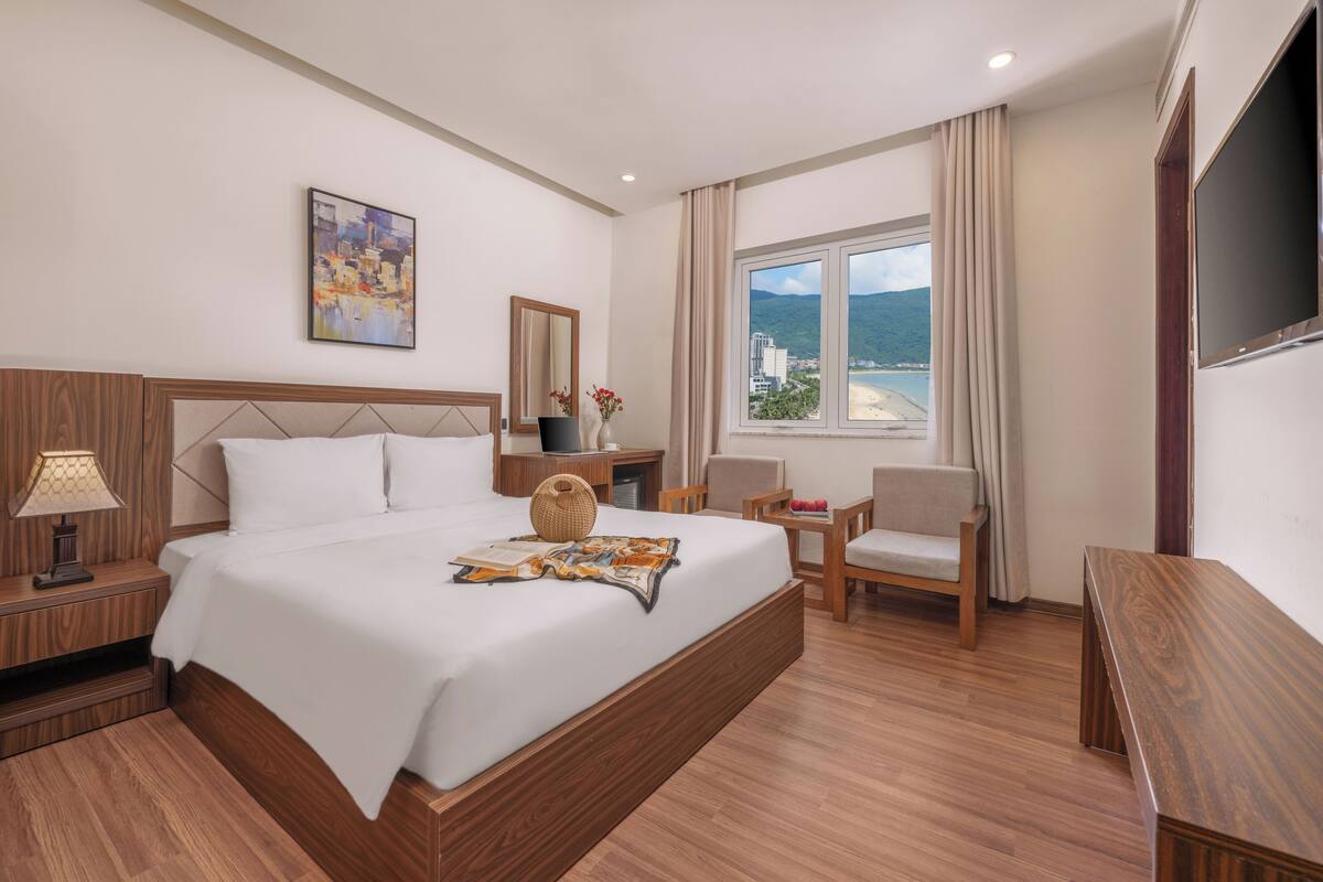 Habitación de hotel moderna con una cama grande, un escritorio, una silla y vistas a la ciudad y las montañas.