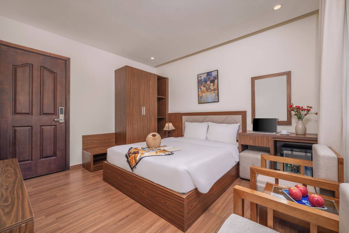 Una habitación de hotel moderna con una cama de madera, un escritorio con una computadora, una silla y una pequeña mesa con manzanas.