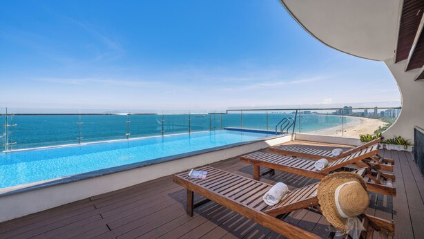 Una terraza con tumbonas de madera, una piscina y vistas a la playa y al océano.
