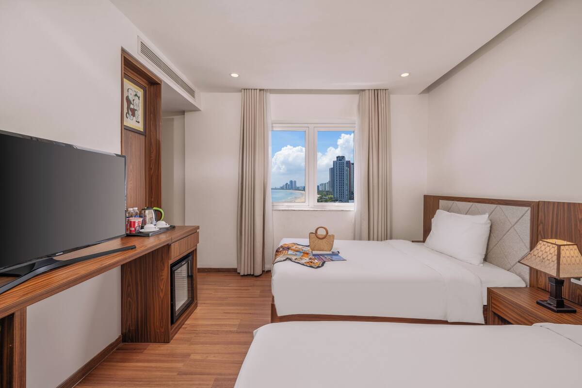 Habitación de hotel con dos camas, televisor, escritorio y ventana con vista a la ciudad.