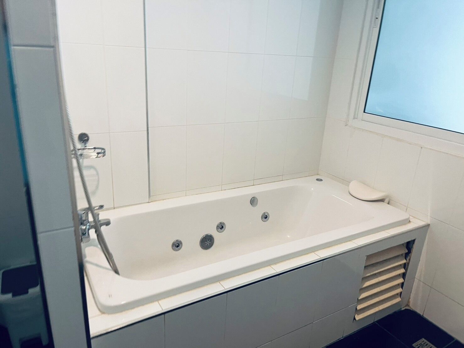 A bathroom with a white bathtub, a shower, and a window.