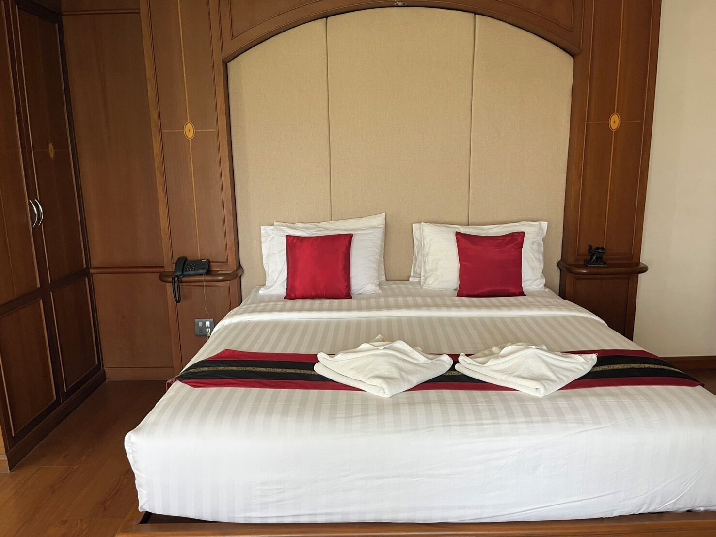 Una cama bien hecha con ropa de cama blanca y roja, un cabecero de madera y un armario de madera.