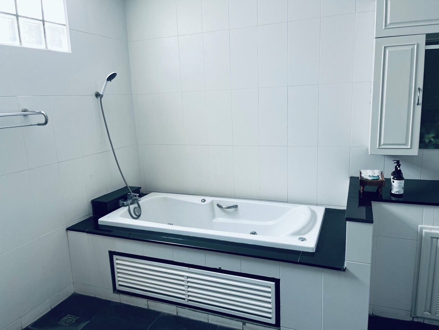 Un baño moderno con una bañera, un asidero, un radiador y un pequeño estante con una botella.