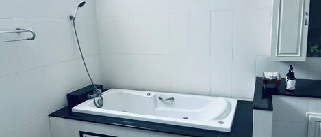 Un baño moderno con una bañera, un asidero, un radiador y un pequeño estante con una botella.