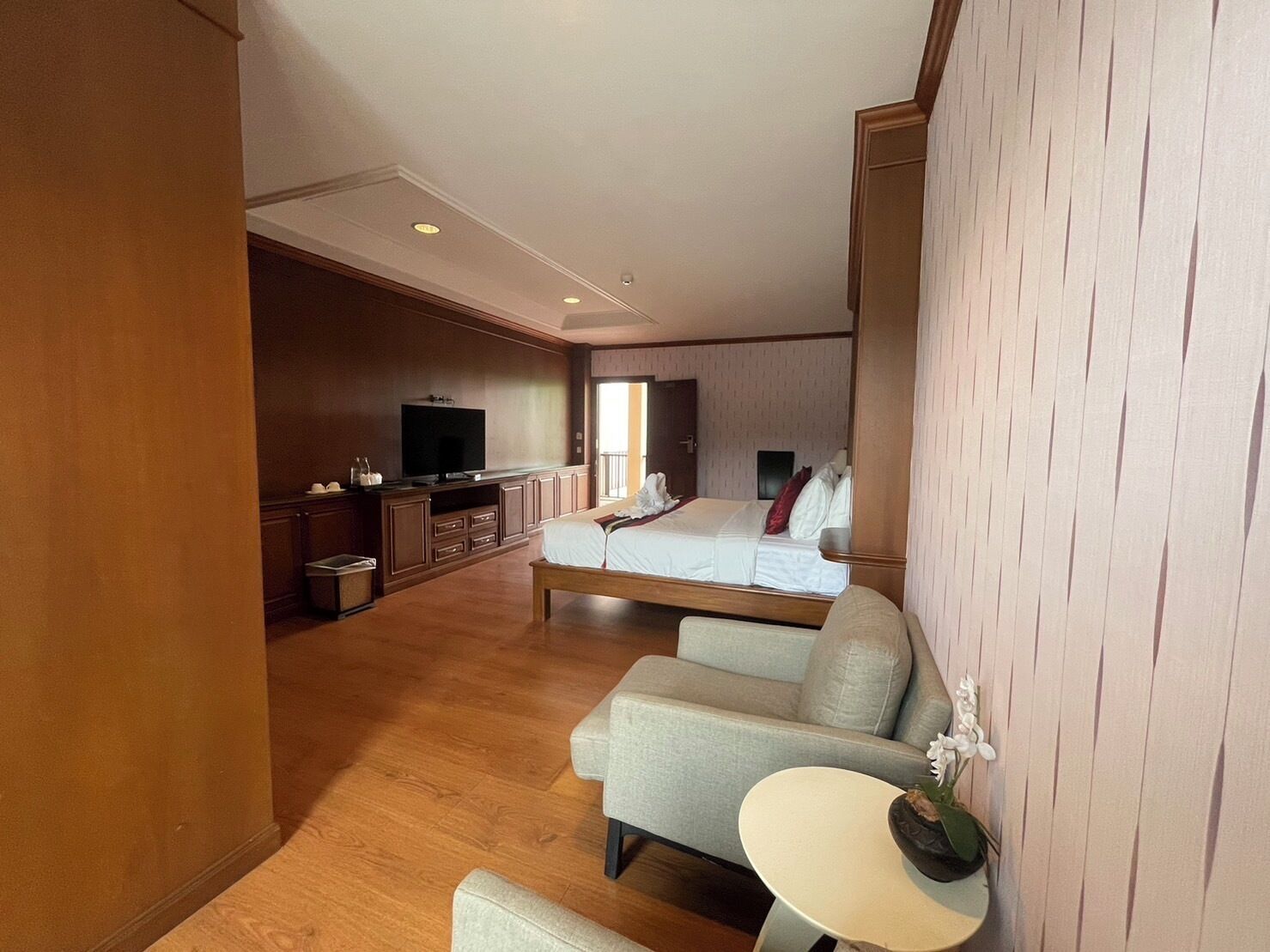 A hotel room with a bed, a sofa, a TV, and a small table with a flower.