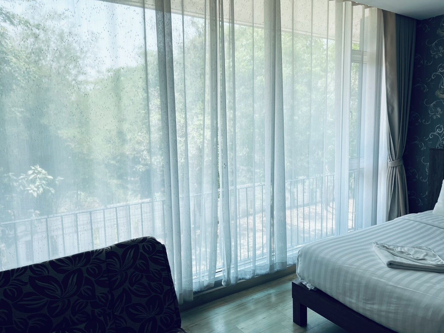 A bedroom with a bed, a bench, and a large window with sheer curtains.