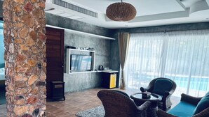 Un moderno salón con un pilar de piedra, mobiliario de mimbre, un televisor de pantalla plana y vistas al exterior.