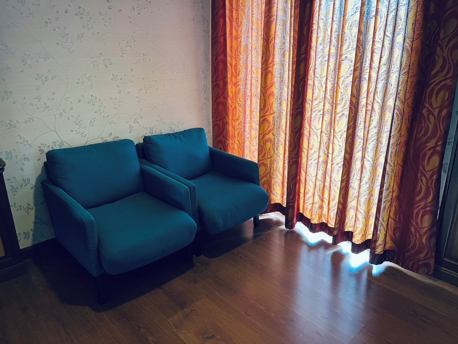 Una habitación con un sofá azul, cortinas estampadas y suelo de madera.