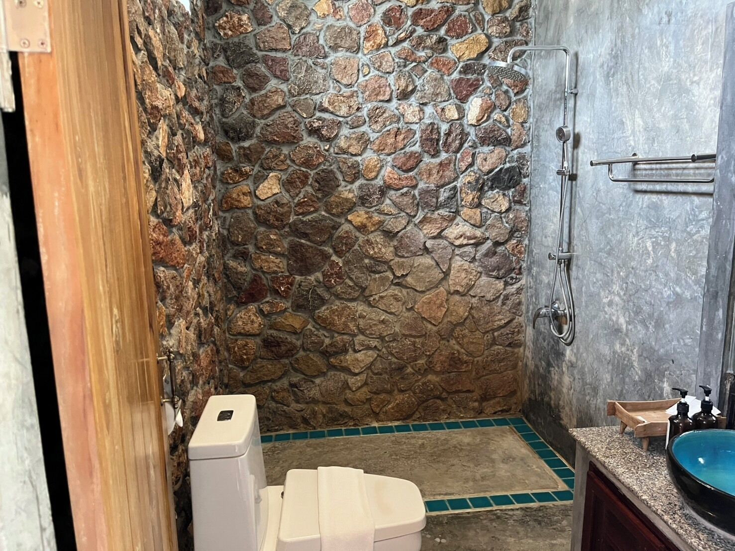 A bathroom with a stone wall, a shower, a toilet, and a sink.