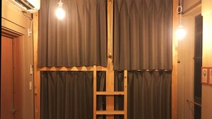 A room with a wooden ladder against a wall with curtains, a door, and a light fixture. - No Borders Hostel (Tokyo)