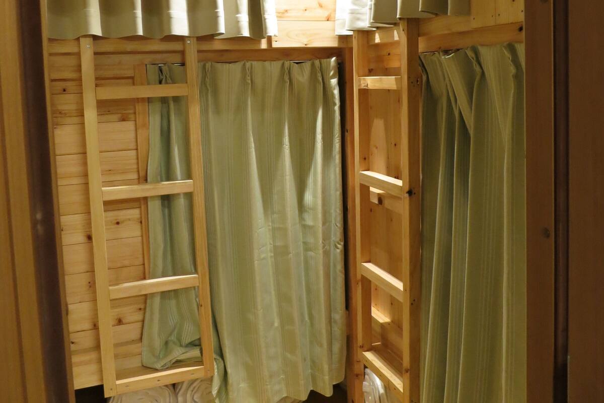 A small, wooden cabin with a loft bed, a ladder, and a shelf with storage bins.