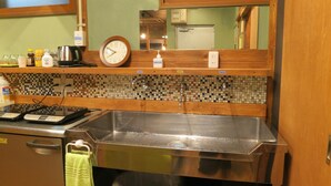 A kitchen with a stainless steel sink, a clock, and a tiled backsplash. - No Borders Hostel (Tokyo)