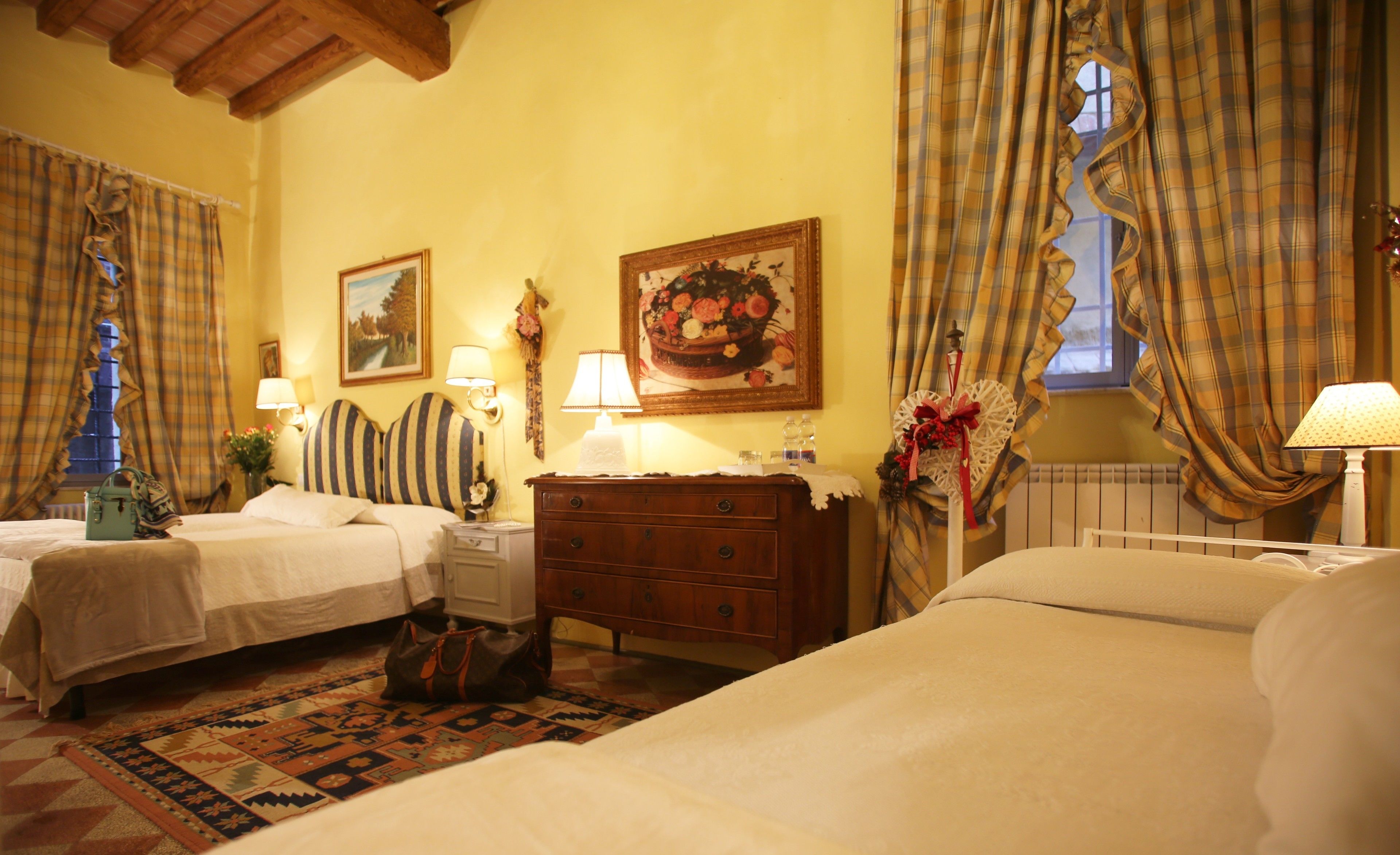 A hotel room with two beds, a wooden dresser, a patterned rug, and a window with curtains.