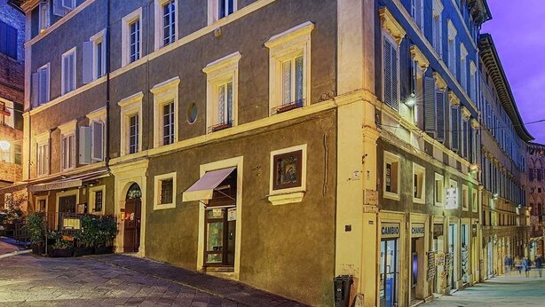 A multi-story building with a classic architectural style, featuring a ground-floor entrance with a canopy and a visible storefront. - B&B Le Aquile (Siena)