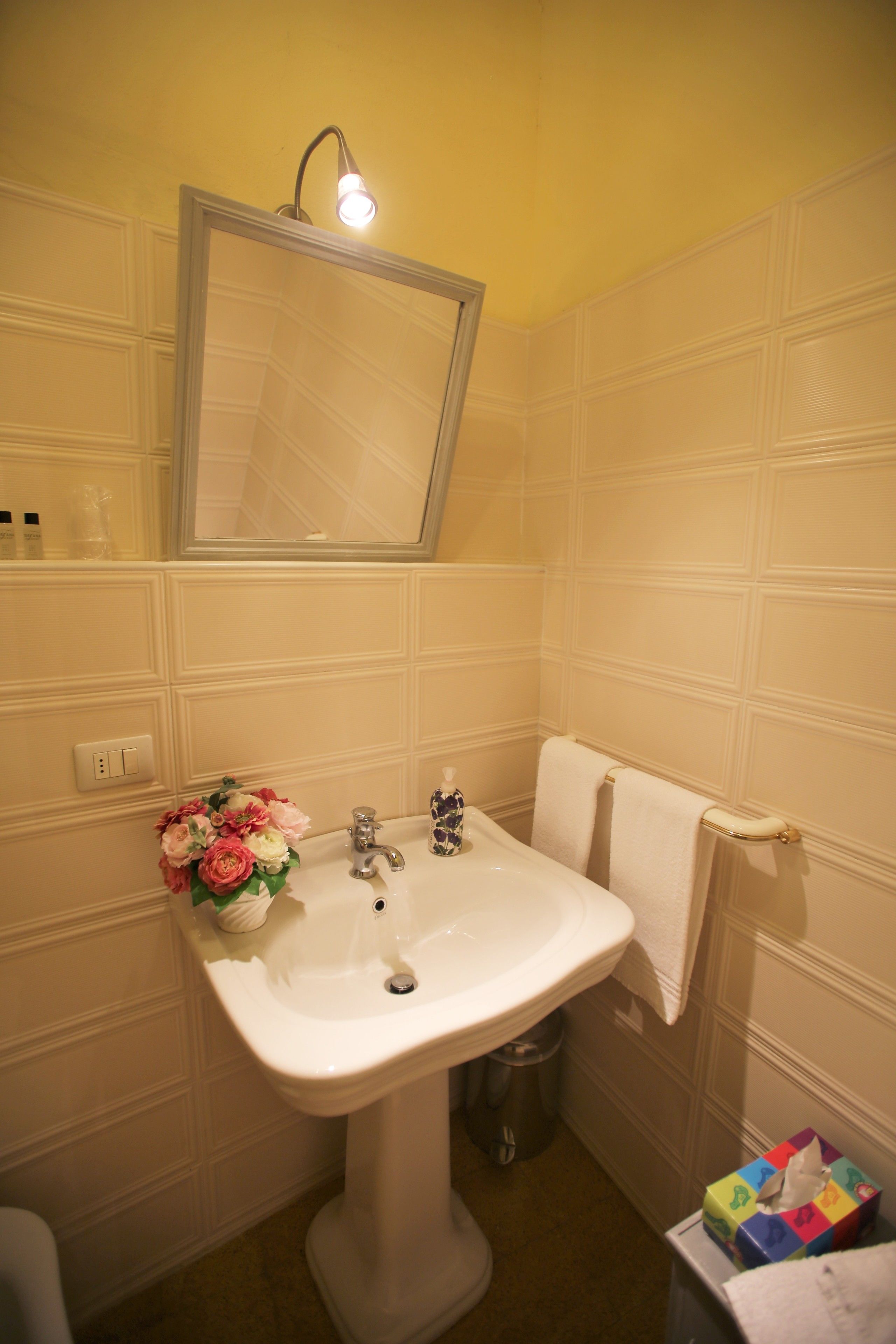 Ein Badezimmer mit einem weißen Waschbecken, einem Spiegel, einer Leuchte und einem Mülleimer.